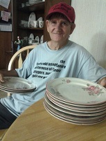 Man holding 3 plates in one hand and 8 plates resting on the table