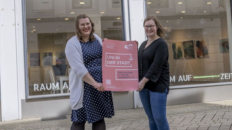 Zwei Frauen zeigen das Werbeplakat für den Pop-up-Store