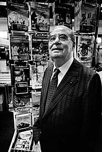 Photographie en noir et blanc d'un homme portant des lunettes et se trouvant dans une librairie.