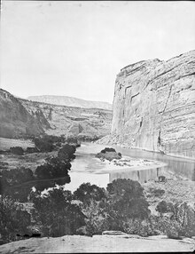 View of two rivers converging behind trees, at the base of a cliff.