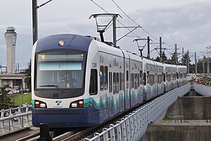 A train with four cars, traveling over a concrete bridge under catenary wires.