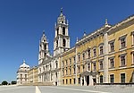 A massive building with yellow facade and two bell towers in the middle