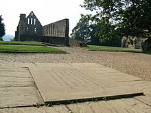 Photo montrant au premier plan une plaque gravée au sol et au fond un édifice religieux en ruine