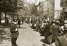 Large number of people standing beside a railway siding with the camp gate in the background