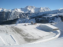 Photographie en couleurs d'une vue prise en hauteur vers l'altiport avec les montagnes dans le fond.