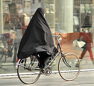 Een vrouw op de fiets in Den Haag die een chador draagt