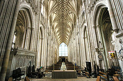 This interior view at Winchester shows the whole length of the nave, which has huge stone piers which appear to comprise clusters of upward-sweeping stone shafts. The stone vault has ribs which sweep up to a point and have been likened to the branches of trees in a forest. The overall effect is visually spectacular.