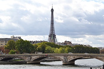 The distinctive green spire of the American Church in Paris in front of the base of the Eiffel Tower