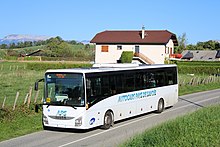 Photographie en couleurs d’un autocar blanc circulant sur une route de campagne au milieu des prés verts.