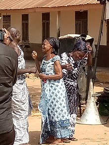 two African women in patterned dresses and head scarfs crying at a funeral