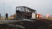 Photograph of the scorched remains of a bus on a roadside