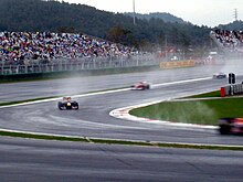 Four Formula One cars are turning left into a corner with spray being lifted from the ground by their tyres.