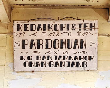 Penggunaan aksara Batak pada papan tanda kedai di Desa Hutajulu, Kabupaten Humbang Hasundutan.