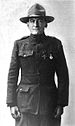 Three-quarters shot of a middle-aged man in a plain military uniform, standing almost at attention. He is wearing a campaign hat and two medals on his chest.