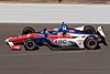 A red, white and blue racing car being driven at high speed on an oval race track