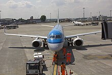 Photo von vier Personen in orage-roter Warnkleidung, die eine Ground-Power-Unit per Kabel an ein Flugzeug anschließen.