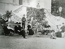 Famille rassemblée devant un perron avec adultes et mobilier de jardin.