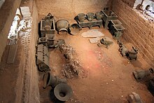 Walled pit with many bronze vessels on the floor and skeletons on top of the side walls