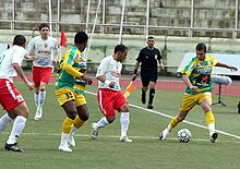 Deux joueurs de football en plein match, un de la JSK l'autre de la JSMB.