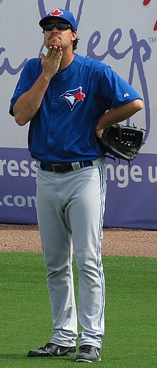 An image of Scott Copeland standing in a Toronto Blue Jays uniform with a baseball glove and sunglasses