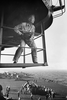 A black and white photograph of a middle aged man in a military uniform and glasses, standing on a gantry above the deck of an aircraft carrier at sea