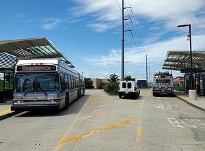 Two silver buses at a bus stop with large canopies