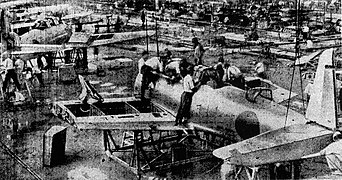 Photo de l'intérieur d'un hangar. Des lignes d'assemblage d'avions sont visibles, et des ouvriers travaillent sur ceux-ci.