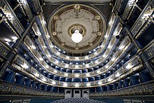 Vue depuis la scène des balcons d'un théâtre à l'italienne, puissamment éclairés. La tonalité de l'ensemble est bleutée.