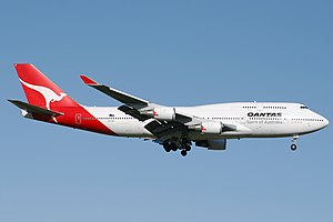 A large white and red four-engine jet airliner with union tail fin, with landing gear extended