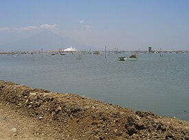 Lake created by mud with steaming mud flow in background.