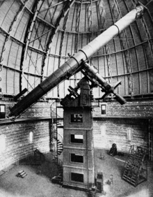 Photographie en noir et blanc d'un grand télescope sous un coupole métallique.