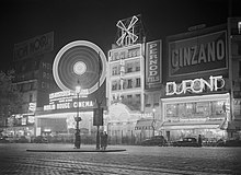 De nuit, derrière une grande place, des façades tape-à-l’œil violemment éclairées de néons.