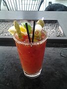 Un cóctel Bloody Mary con varias decoraciones: gajos de limón y de lima, brocheta de aceitunas y cebolla mini y un espárrago.