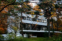 Große, offene Innenräume und Fensteröffnungen mit einer Terrasse zum Garten und auf dem Dach gewähren Ausblick auf den das Gebäude umschließenden Kiefernwald.