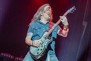 Troy McLawhorn wearing jeans and a denim vest over a dark t-shirt, playing guitar onstage