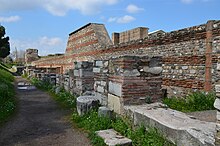 Ruined brick buildings along a street, slightly overgrown by grass at the edges.