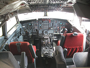 Photographie en couleurs de l'intérieur d'un cockpit montrant le tableau de bord et les sièges des pilotes.