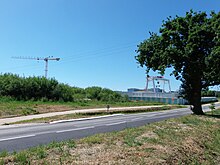 Photo d'une route entourée d'herbe et de végétation, avec un arbre au premier plan et une grue en second plan.