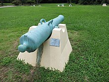 Cannon with green patina mounted on a concrete pedestal.