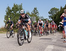 A large group of cyclists racing along a road with a crowd watching on the right hand side