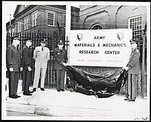 Army officials at Watertown Arsenal unveil a new sign that reads “Army Materials & Mechanics Research Center” in a large dark font and “Army Materiel Command” underneath in a smaller, lighter font.