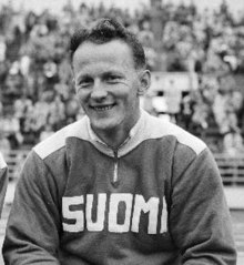 Schwarzweißfoto: Toivo Hyytiäinen sitzt im Trainingsanzug mit der weißen Aufschrift Suomi.