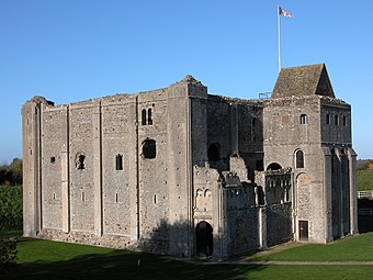 A large square castle keep of pinkish-grey stone, with a projecting entrance tower, has architectural details to its windows, mouldings and stonework.