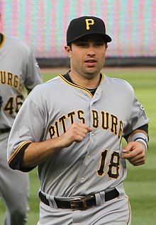 A light-skinned man in a gray baseball uniform with "PITTSBURGH" on the chest and a black baseball cap with "P" in yellow on it jogs towards the camera.