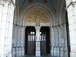 Le porche et l'entrée. Sur le pilier central est placée une statue de Notre-Dame de Lourdes. Sur le tympan du portail sont représentés le Christ pantocrator et le tétramorphe