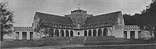 Two colonnaded wings branch diagonally each side from a squat central steeple