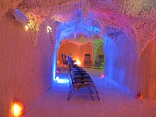 chaises longues dans une salle aux murs, sol et plafond recouverts de sel, décorés de stalactites et éclairés en rose, bleu et vert