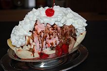 Banana split in a metal dish with vanilla, strawberry and chocolate ice creams topped with whipped cream and a maraschino cherry