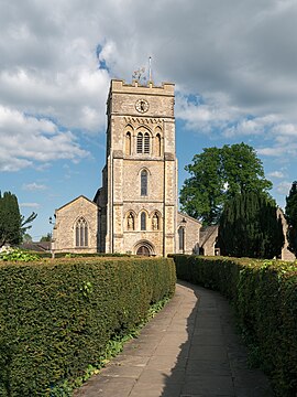 St. Peter's Church, Brackley, in 2023. View from a western direction in afternoon light, with hedges in the foreground lining the path to the main entrance.