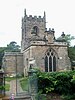 A stone church seen from the east. It has a three-light east window, over which is a sundial, and beyond it is a battlemented tower